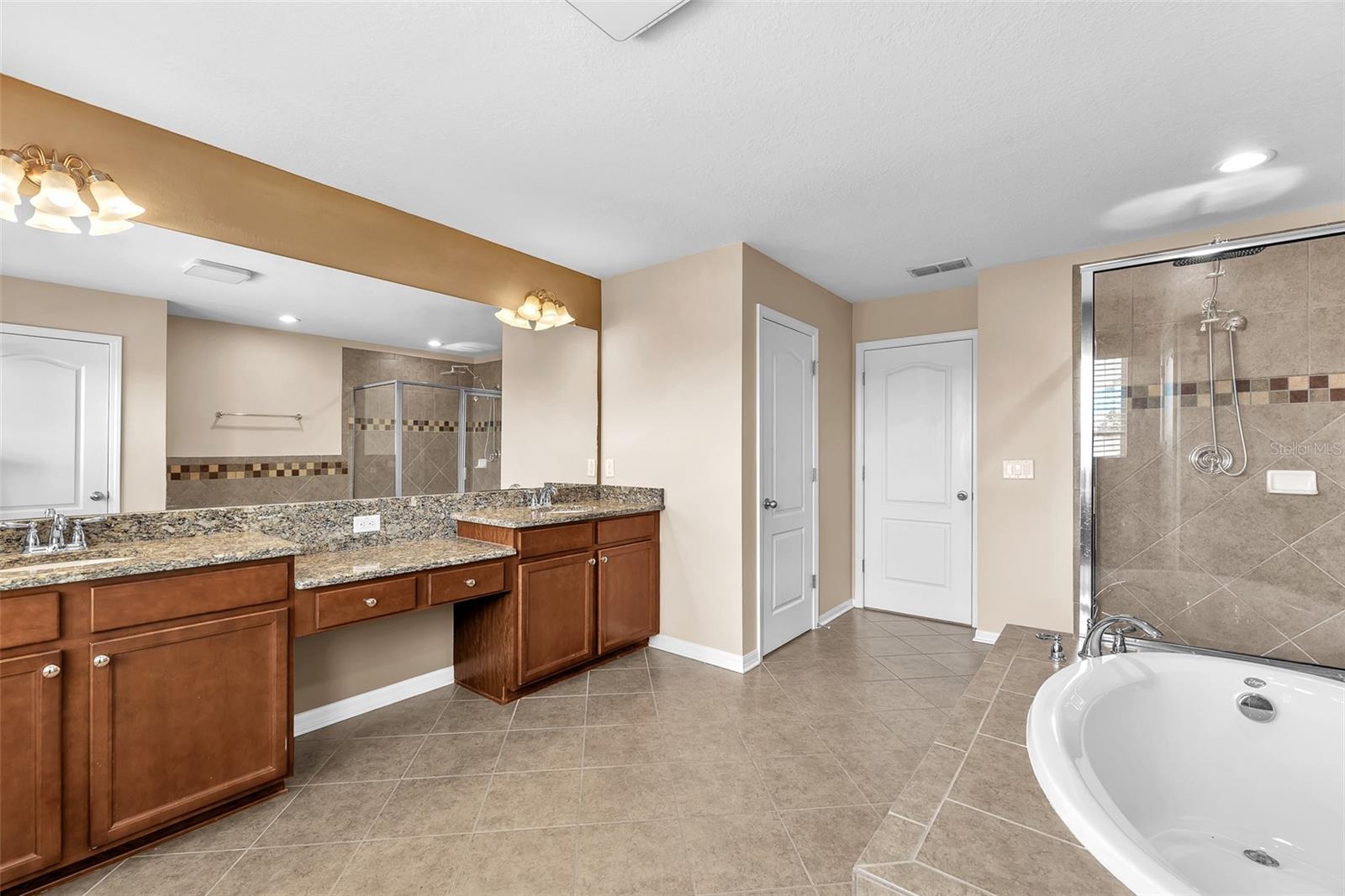 This spa-like en-suite bath is complete with a large vanity with dual sinks and a makeup vanity, a soaking tub, separate shower, and a private water closet.