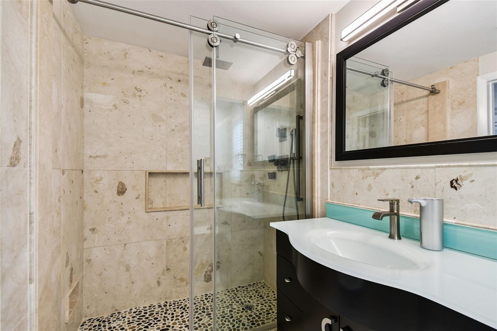 Renovated bathroom with custom tile work and river rock shower floor. How about those shower doors?