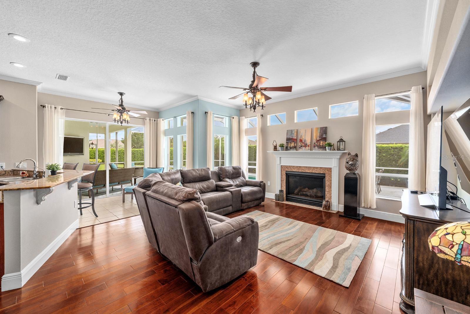 The Great Room features a gas fireplace and mantle, hardwood flooring, crown molding, and lighted ceiling fans.