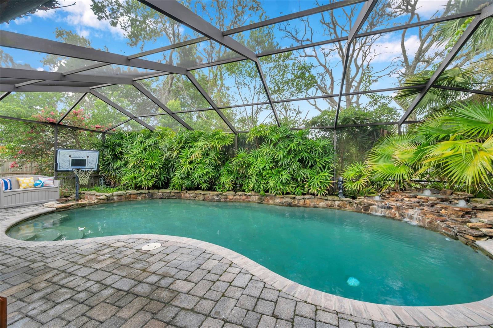 Screen enclosed pool with rock waterfall, pavers, and huge covered patio