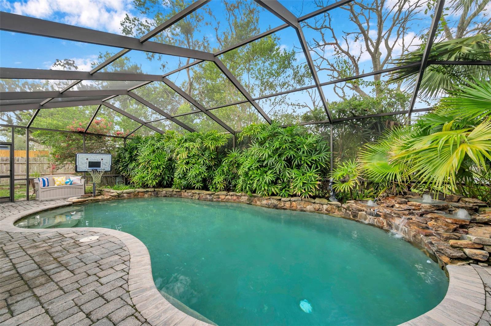 Screen enclosed pool with rock waterfall, pavers, and huge covered patio