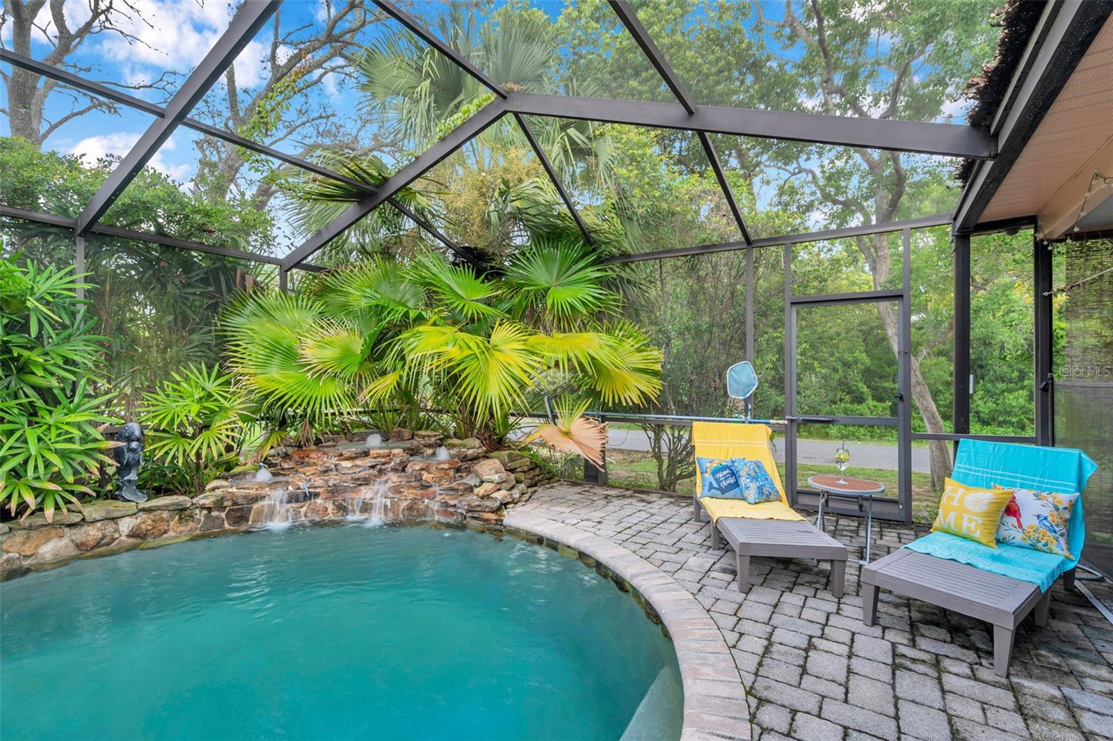 Screen enclosed pool with rock waterfall, pavers, and huge covered patio