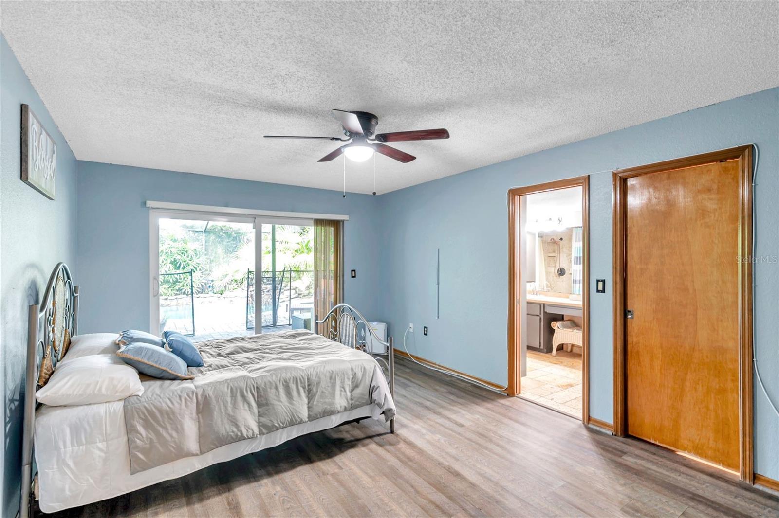 Primary bedroom features a Sliding Glass Doors to the Pool/Patio, Ensuite Bathroom, Ceiling Fan, and large Walk-In Closet