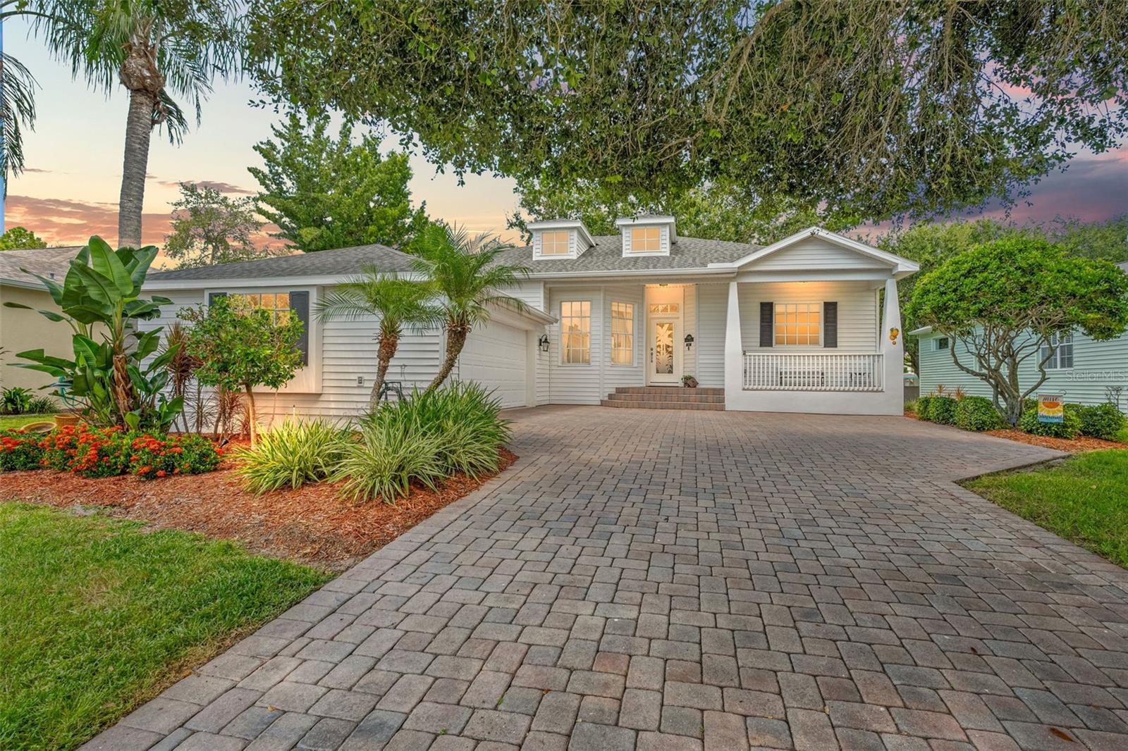 Evening glow highlights the paver driveway, manicured garden beds, and the home’s inviting façade.