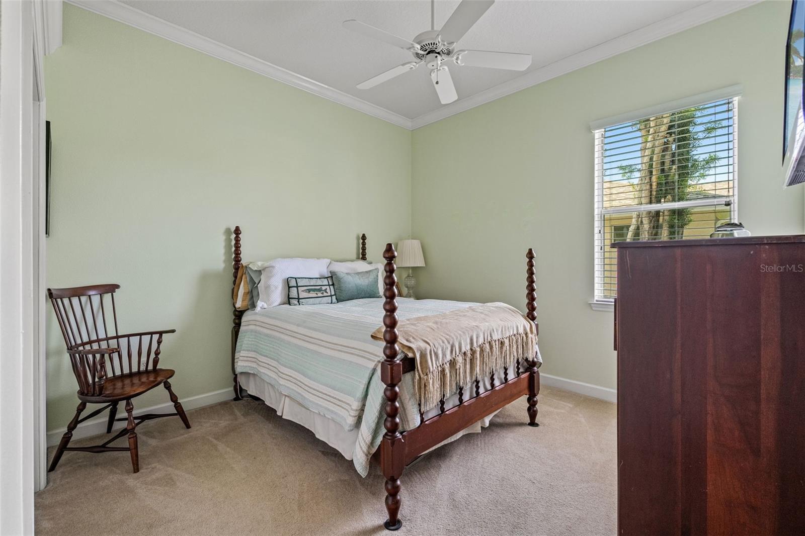 Bright guest bedroom with soft green walls, crown molding, and large window for natural light.
