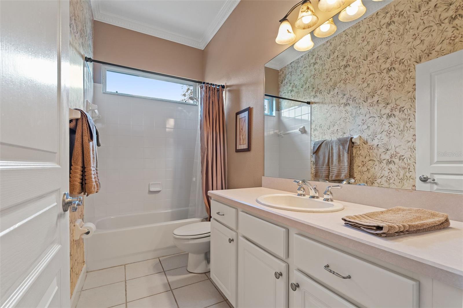 Full bath with single vanity, tub/shower combo, and decorative wallpaper accent.