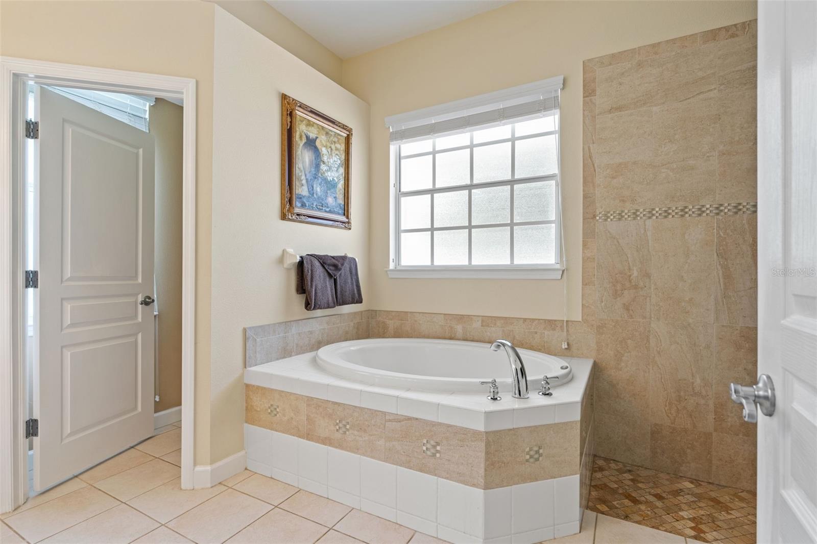 Spa-like bathroom featuring a soaking tub, walk-in shower with tile accents, and frosted window for privacy.