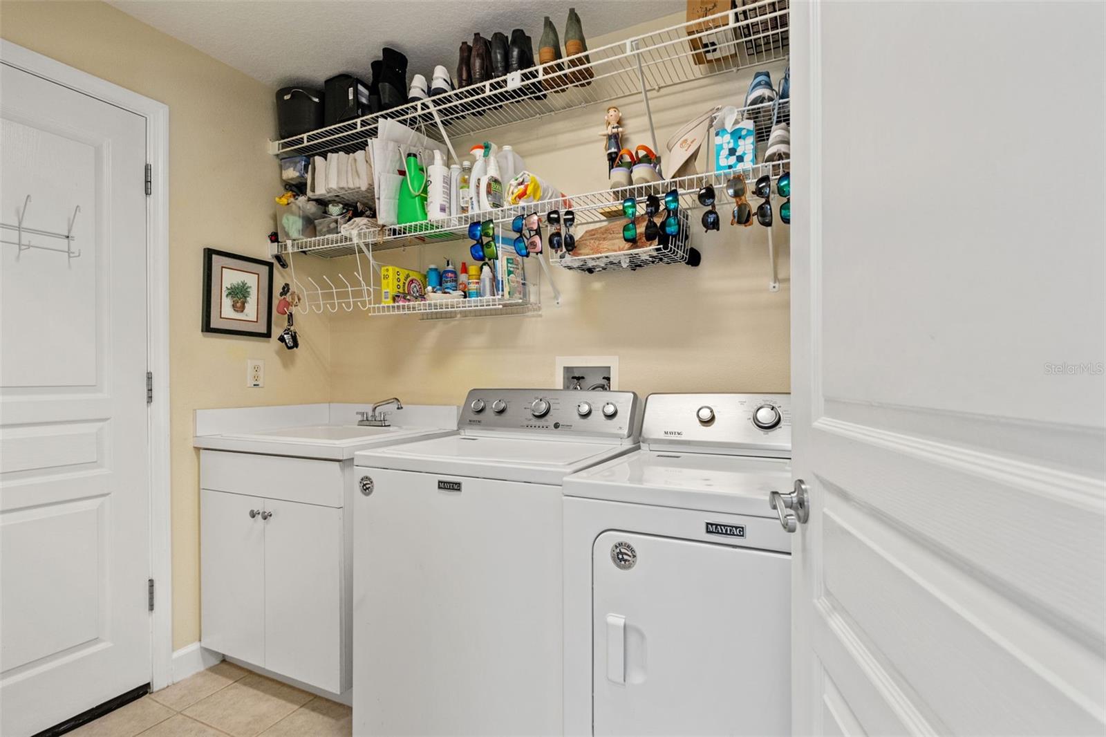Convenient laundry room with washer, dryer, utility sink, and overhead shelving for storage.