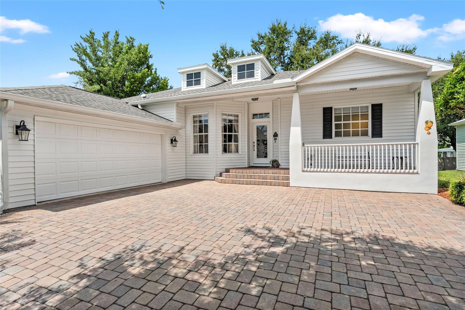 Brick paver entryway, classic white railing, and decorative glass door create a warm welcome.