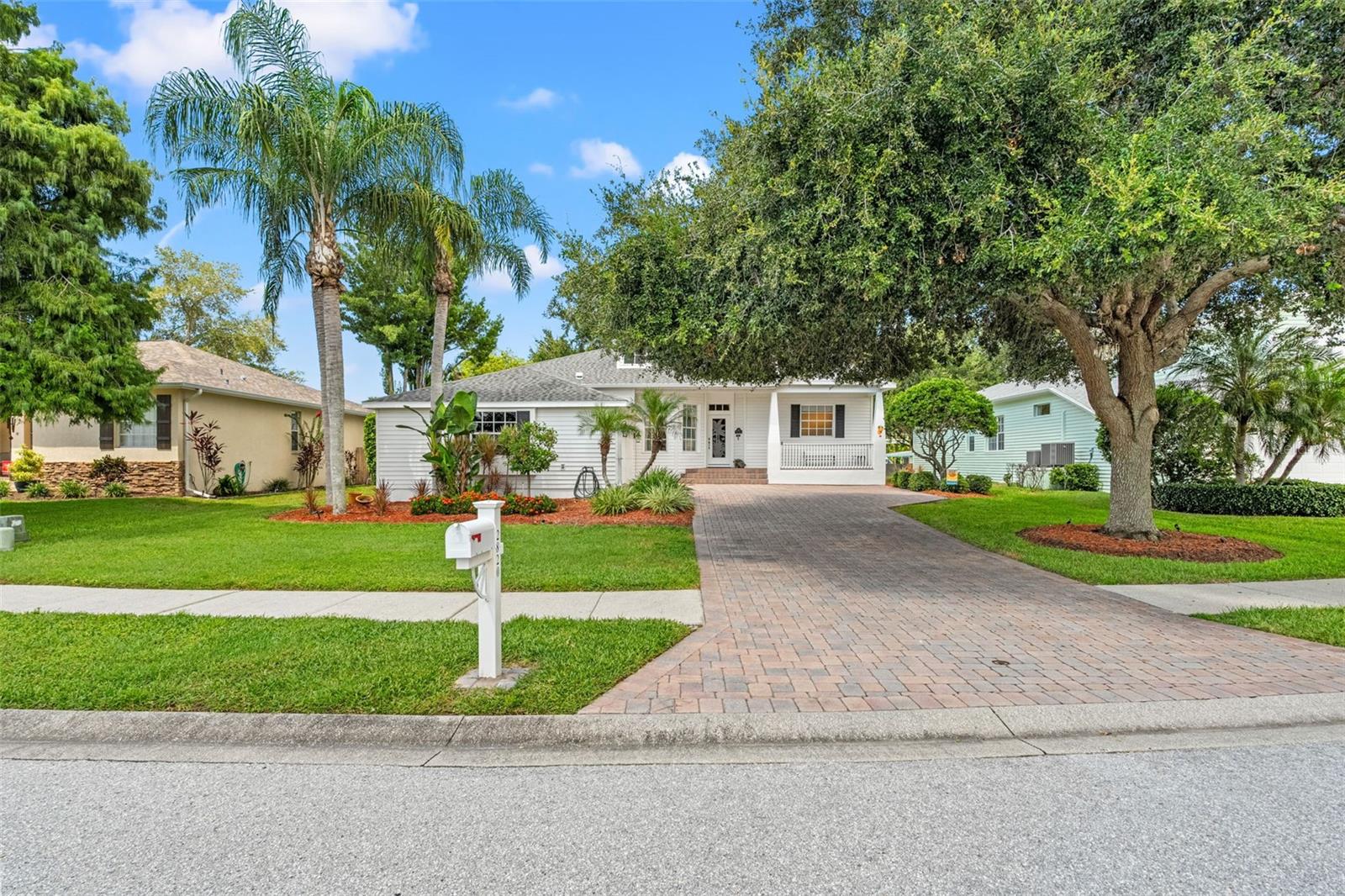 Charming curb appeal with mature trees, tropical landscaping, and a paver driveway leading to the covered front porch.