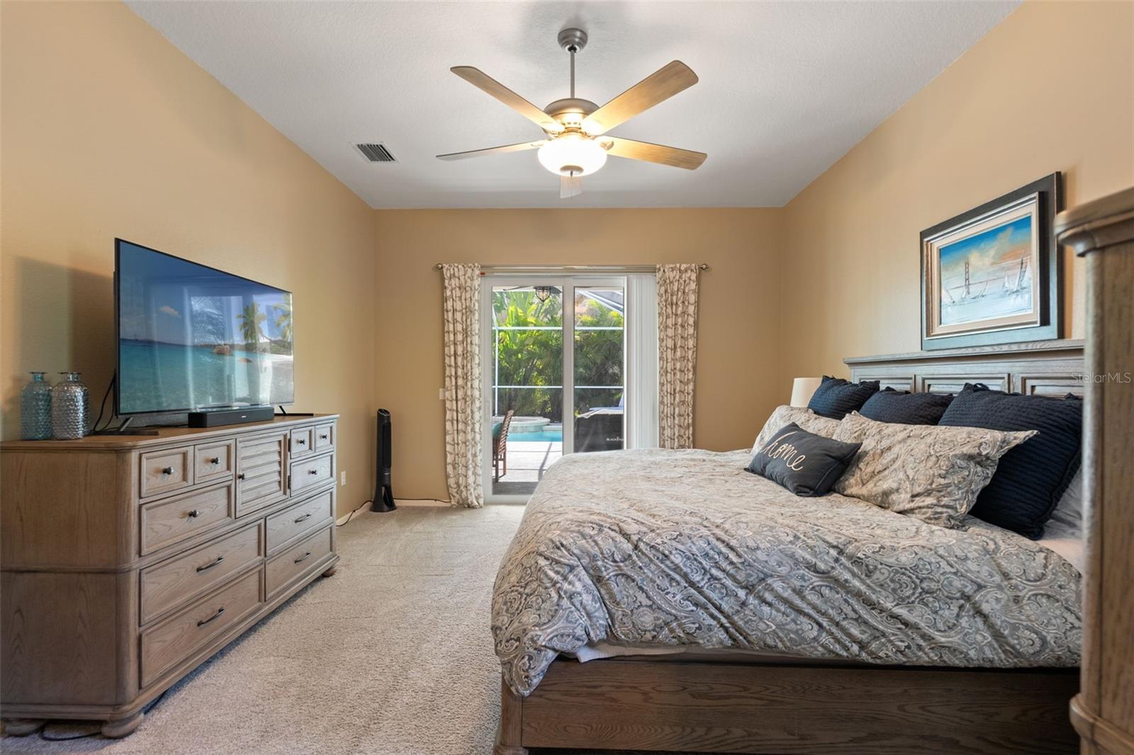 Spacious and serene, the primary suite features warm wall tones, soft carpeting, and direct access to the screened lanai and pool—creating a private retreat just steps from outdoor leisure.