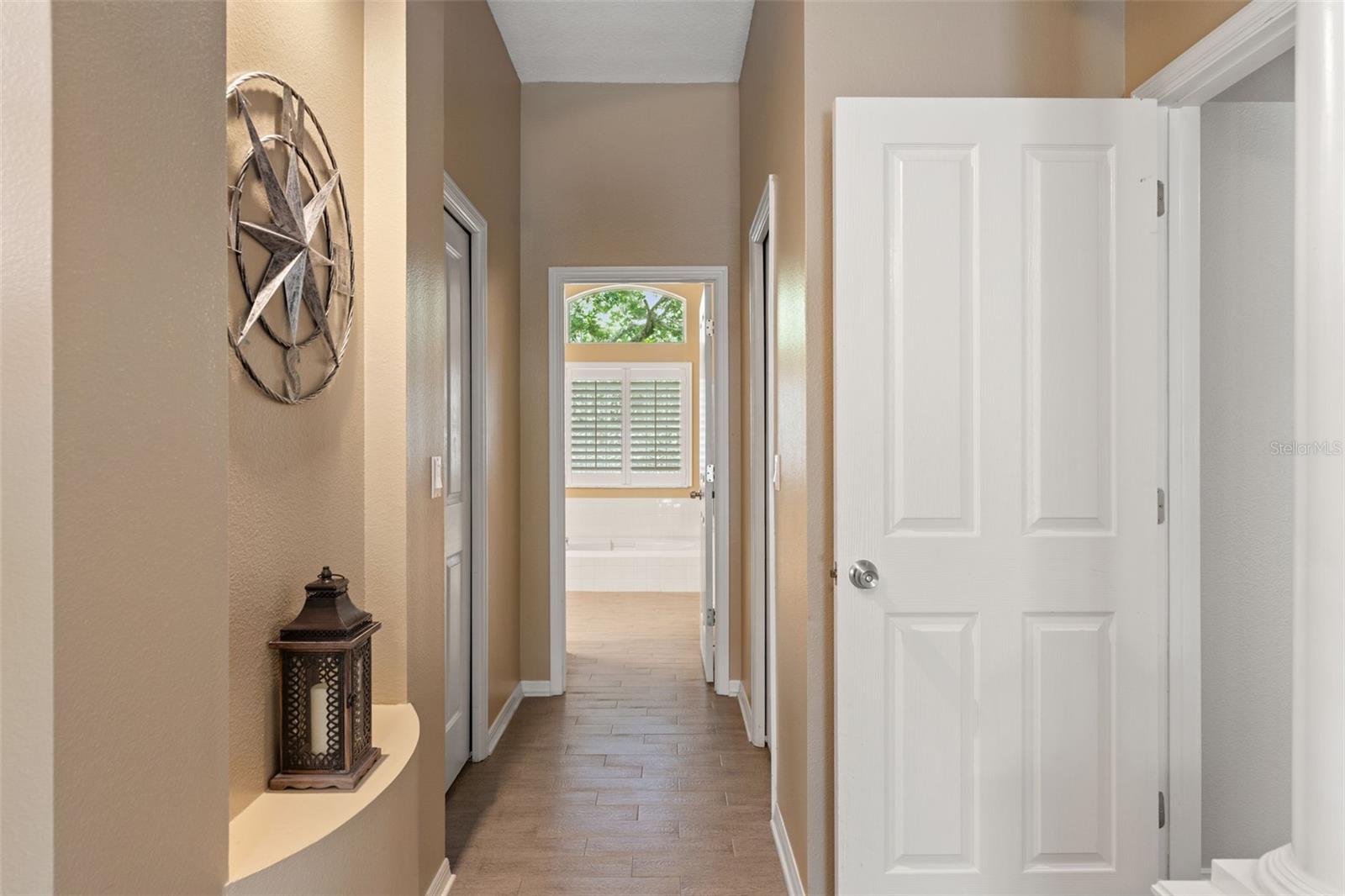 A private hall connects the bedroom to the ensuite bathroom, featuring built-in display niches and views of the soaking tub framed by natural light.