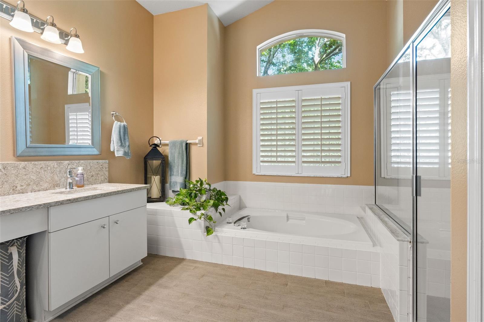 The ensuite bath offers a spa-like experience with a large soaking tub, plantation shutters, dual vanities with stone countertops, and warm finishes throughout.