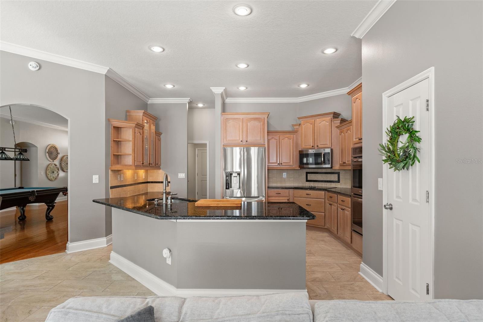 This functional kitchen showcases warm wood cabinetry, granite countertops, stainless steel appliances, and a large peninsula with bar seating.