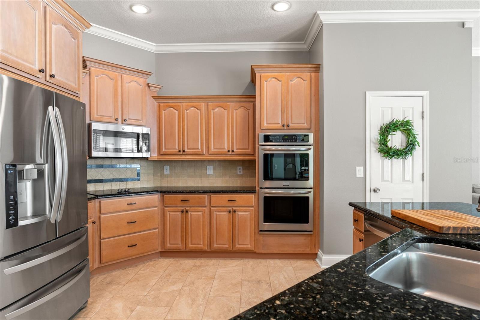 A closer look at the double wall ovens and large pantry with decorative door. Recessed lighting and neutral tile backsplash complete the polished design.