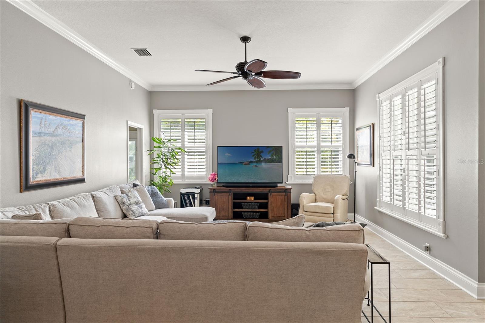 A bright, inviting space with tile flooring, neutral paint tones, and multiple windows with plantation shutters. Perfect for gathering or unwinding.