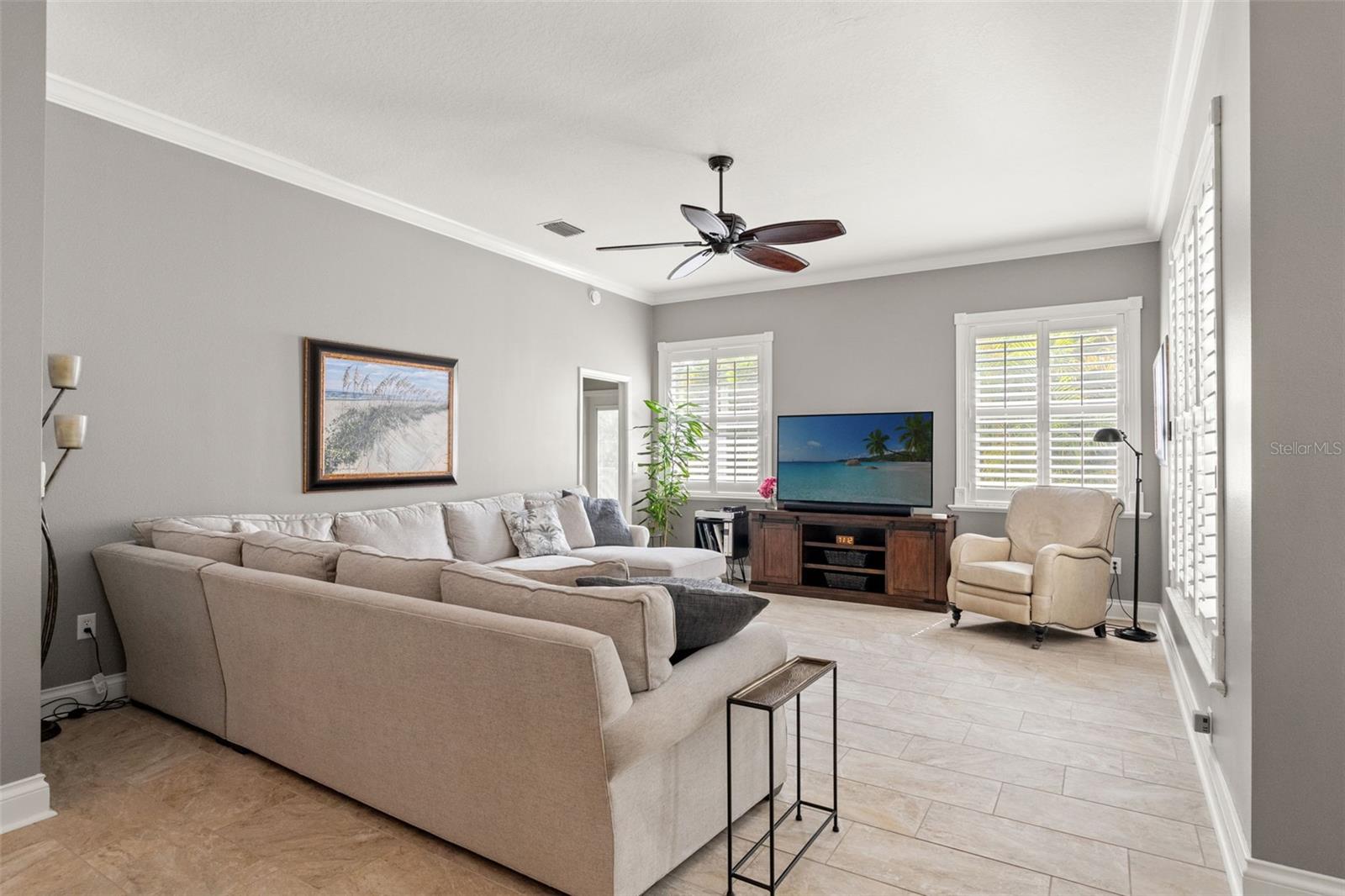 This view highlights the sectional seating area and media setup beneath a tray ceiling with crown molding and ceiling fan.