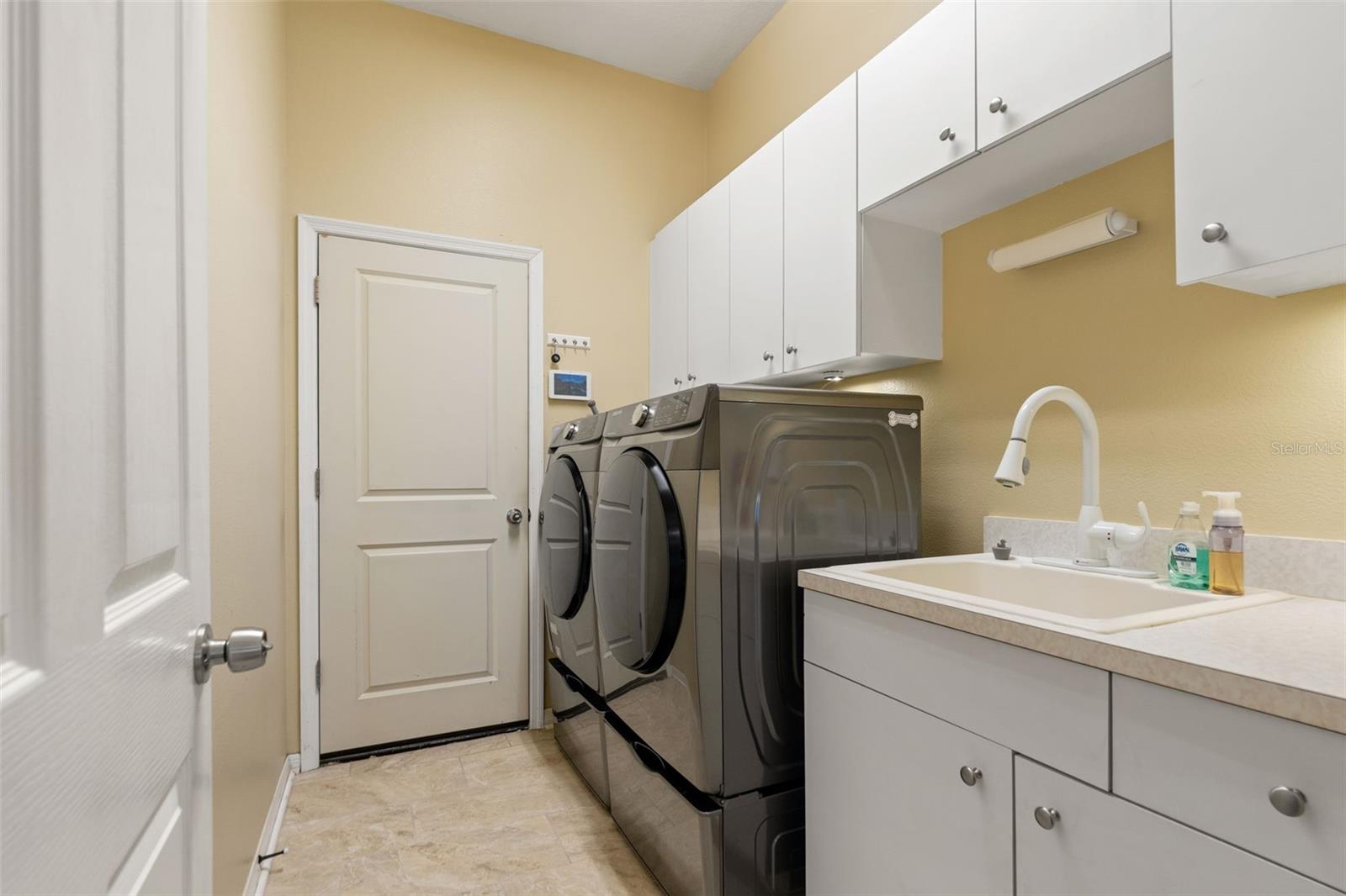 Spacious laundry area equipped with modern front-load washer and dryer, utility sink, and ample upper cabinetry for extra storage.