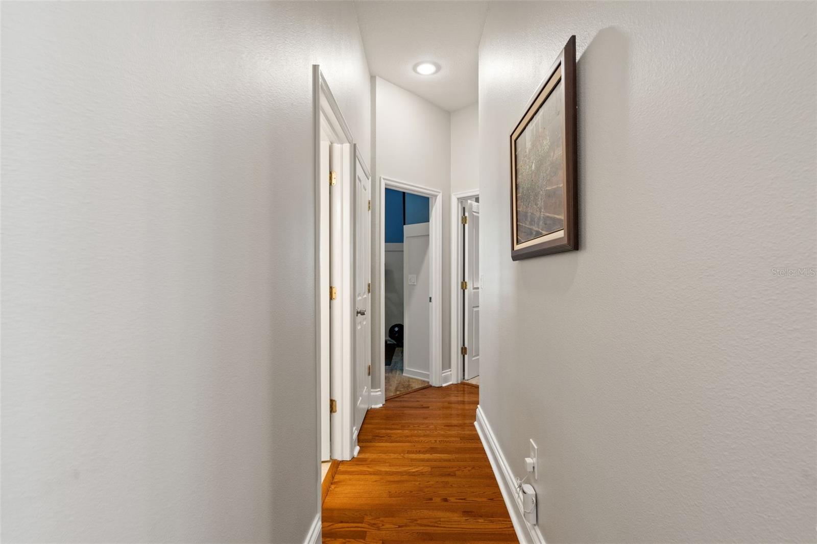 This hallway offers access to additional bedrooms and baths, featuring wood flooring, crisp white trim, and recessed lighting for a clean, polished look.