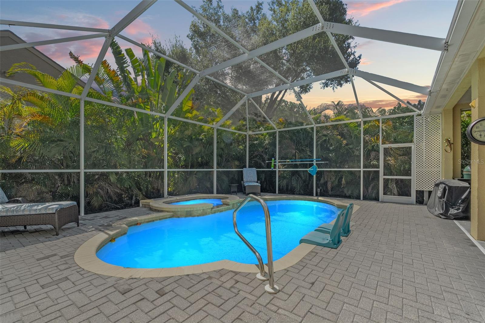 This inviting saltwater pool and raised heated spa are beautifully lit for evening enjoyment, surrounded by privacy landscaping and enclosed in a screened cage.