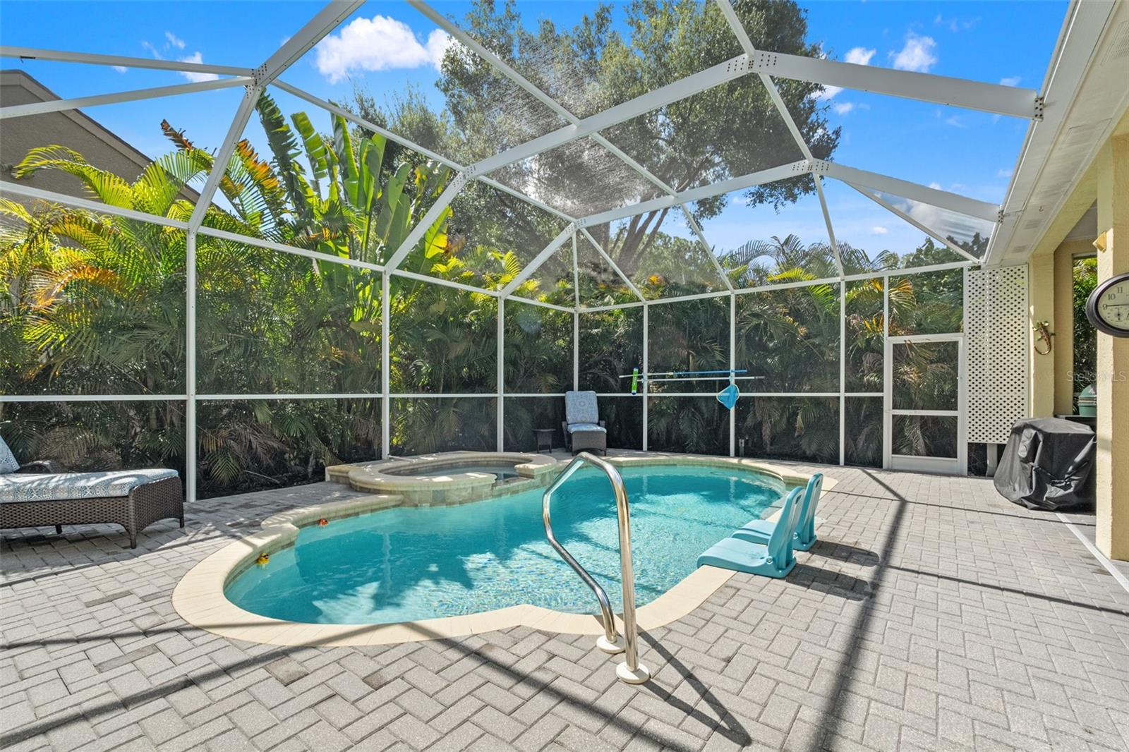 The resort-style pool and spa are framed by lush tropical foliage, offering privacy and serenity in a fully screened enclosure.