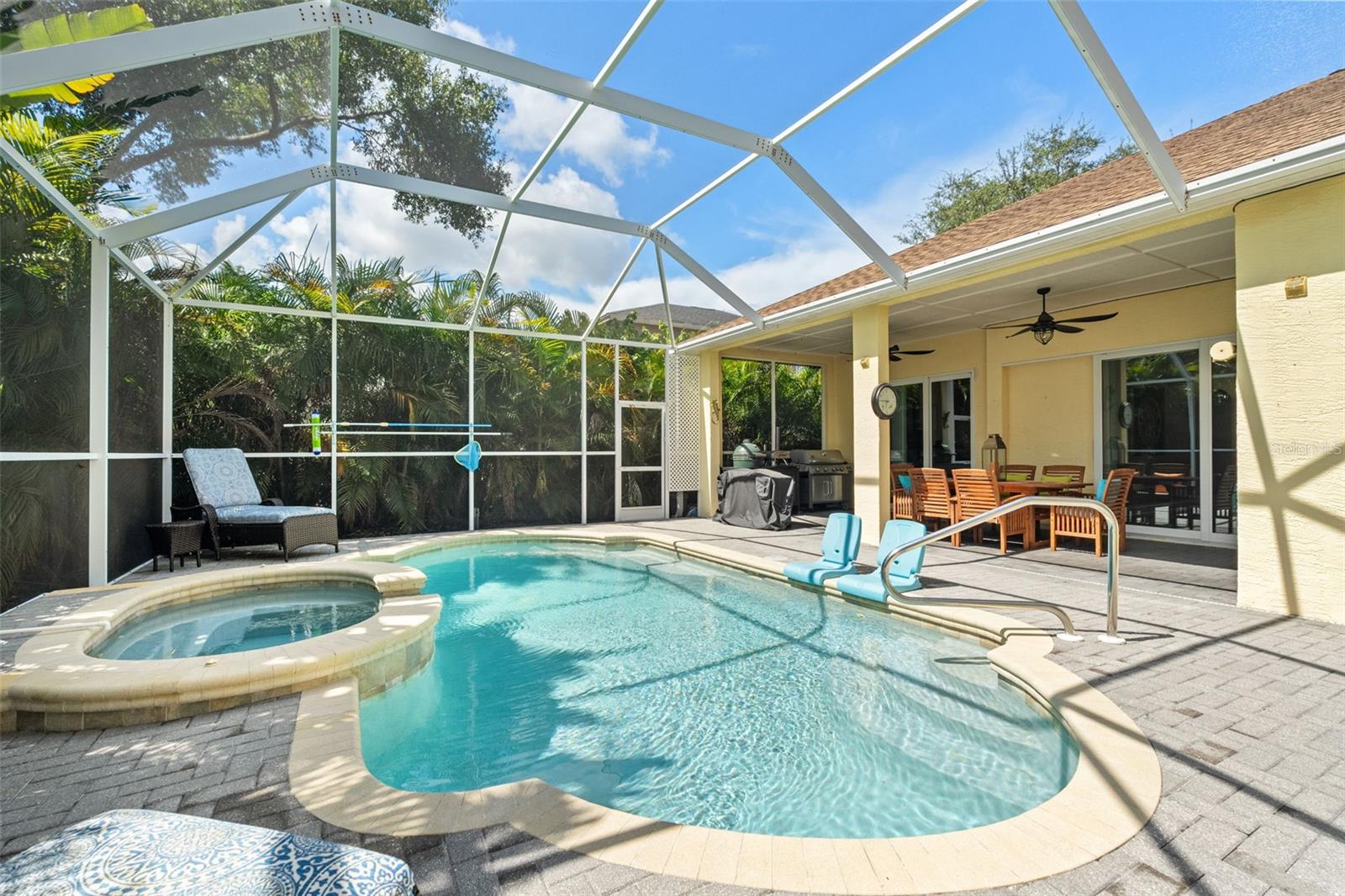 A full view of the resort-style outdoor space showcases the inviting pool, covered lanai, and lush privacy landscaping all around.