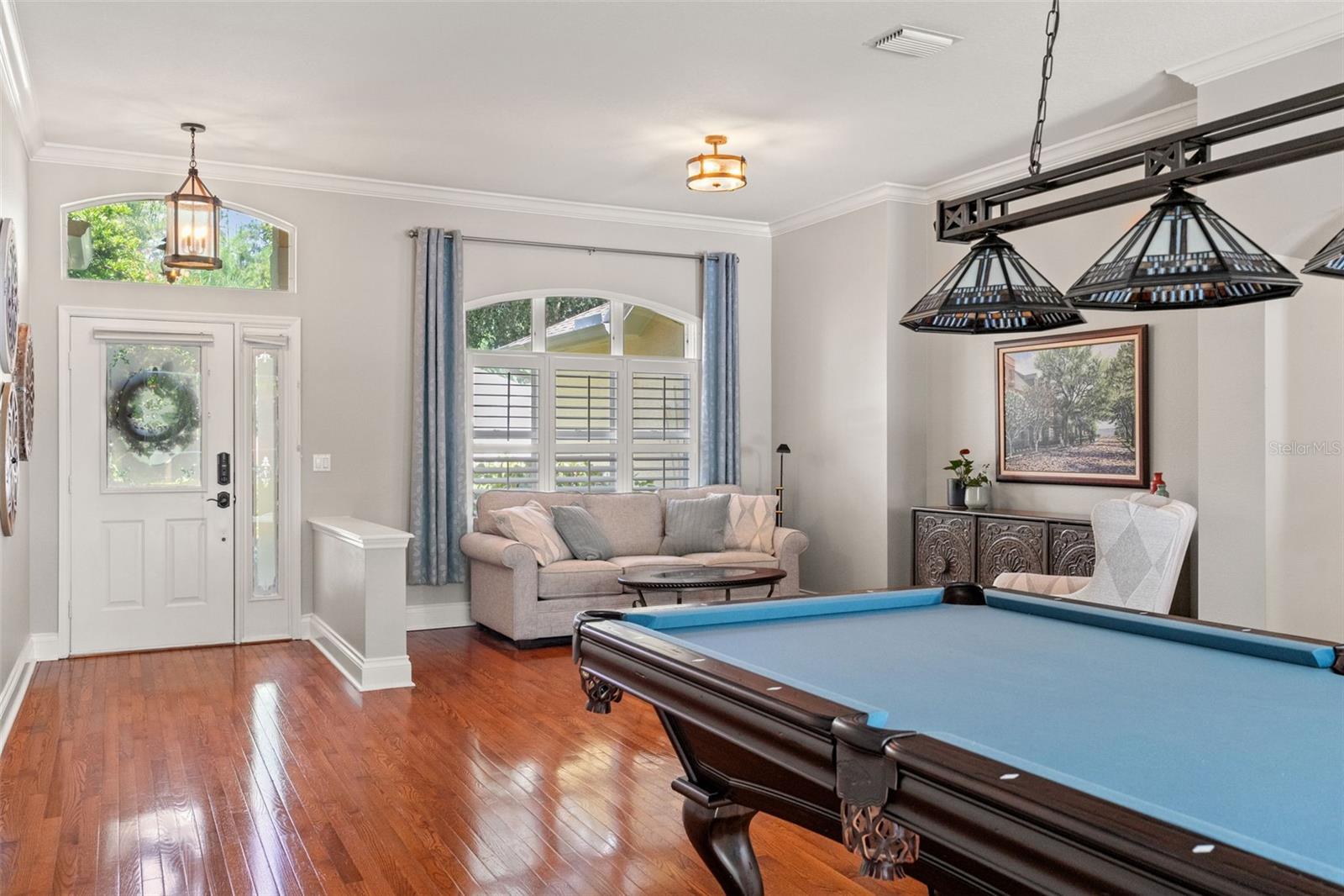 Welcoming entryway flows into the vibrant game (or dining room) and family room, with hardwood flooring, decorative lighting, and arched walkways enhancing the home's inviting feel.