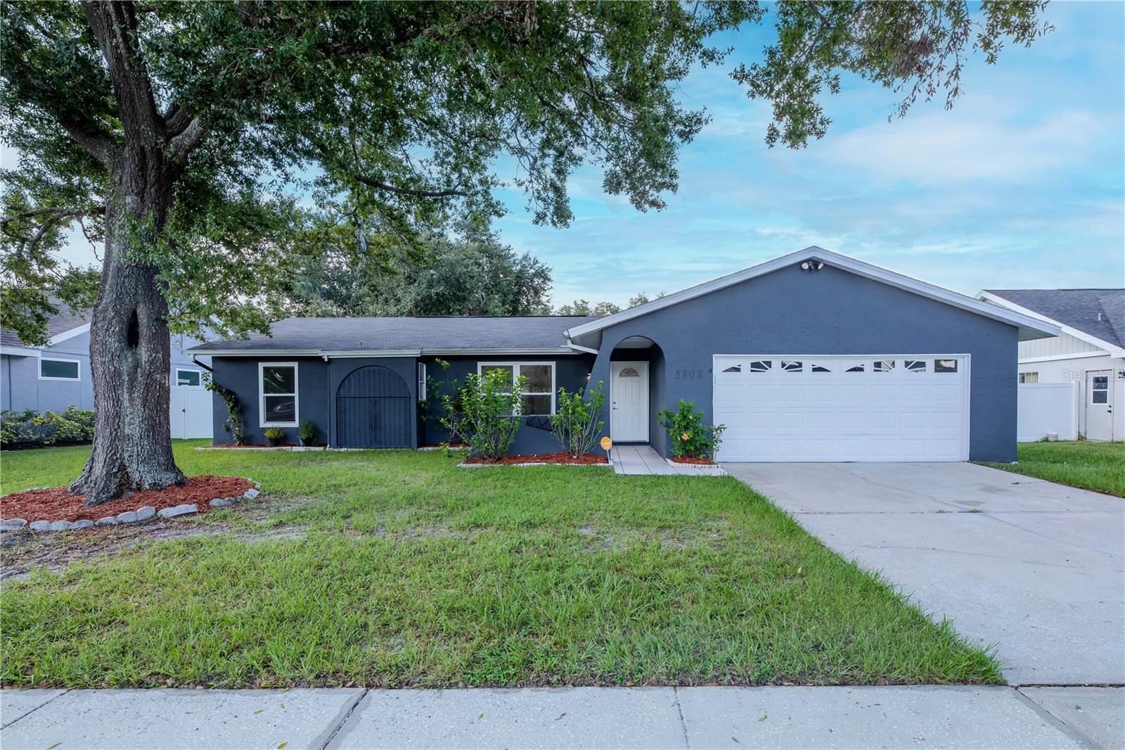 Welcoming curb appeal in a friendly neighborhood, featuring a freshly painted exterior, shade tree by the entry, and a wide driveway framed by a lush green lawn