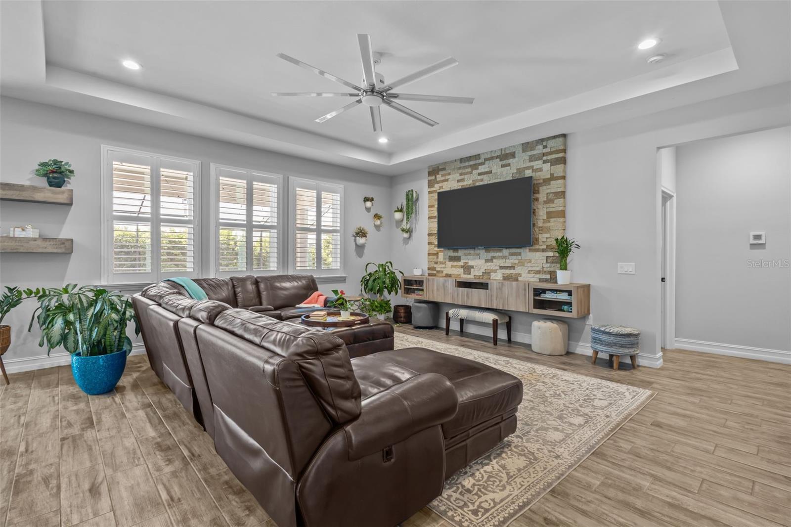 Living room with plantation shutters, tray ceiling, and stone feature wall