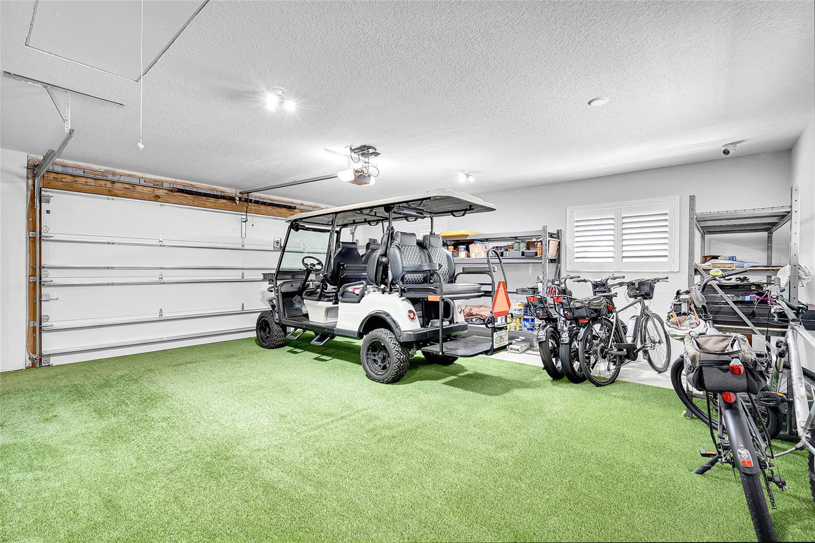 Two car garage with AstroTurf flooring and plantation shutters on the windows.  Attic access pull down ladder