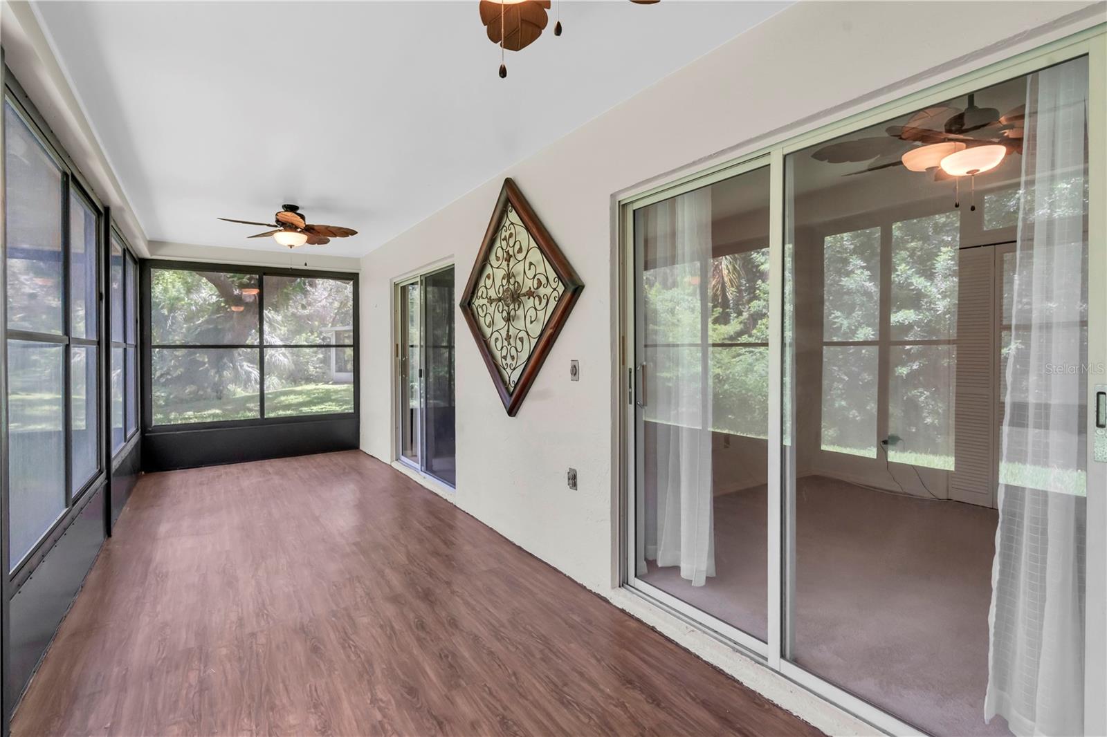 DOUBLE SLIDERS ON THE RIGHT LEAD TO THE SECOND BEDROOM; DOUBLE SLIDERS IN THE DISTANCE ON THE RIGHT LEAD INTO THE PRIMARY BEDROOM; THIS IS A CORNER UNIT SO YOU GET SOME EXTRA GREEN GOODNESS ON THE END OF THE BUILDING; LARGE SCREENED LANAI WITH NEWLY LAID LAMINATE FLOORING AND VINYL WINDOWS; SCREEN DOOR LEADING OUTSIDE IS NOT VISIBLE IN THIS SHOT  (1377 MCMULLEN BOOTH RD)