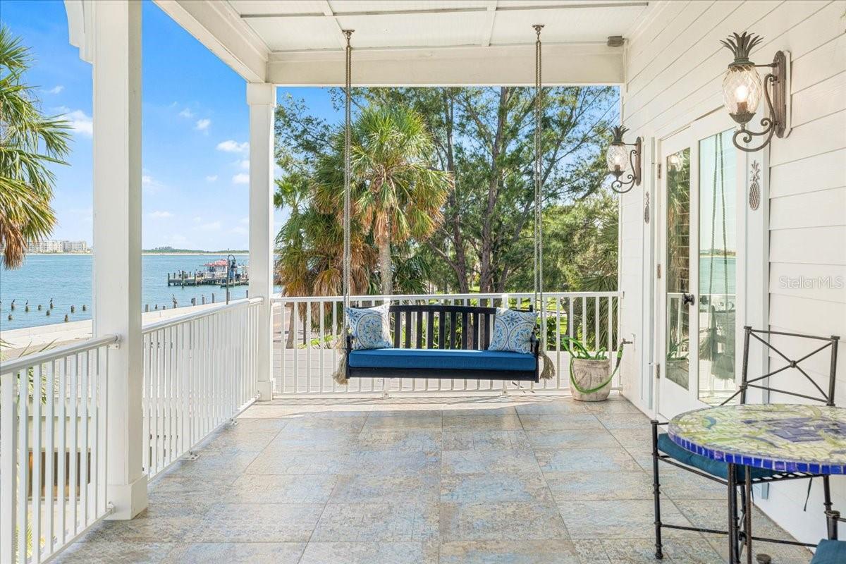 2nd Floor:  Second Floor Patio, Hinkley Pineapple lighting, Porch Swing with cushions, decorative pillows, and a unique tiled table with chairs pictured in forefront