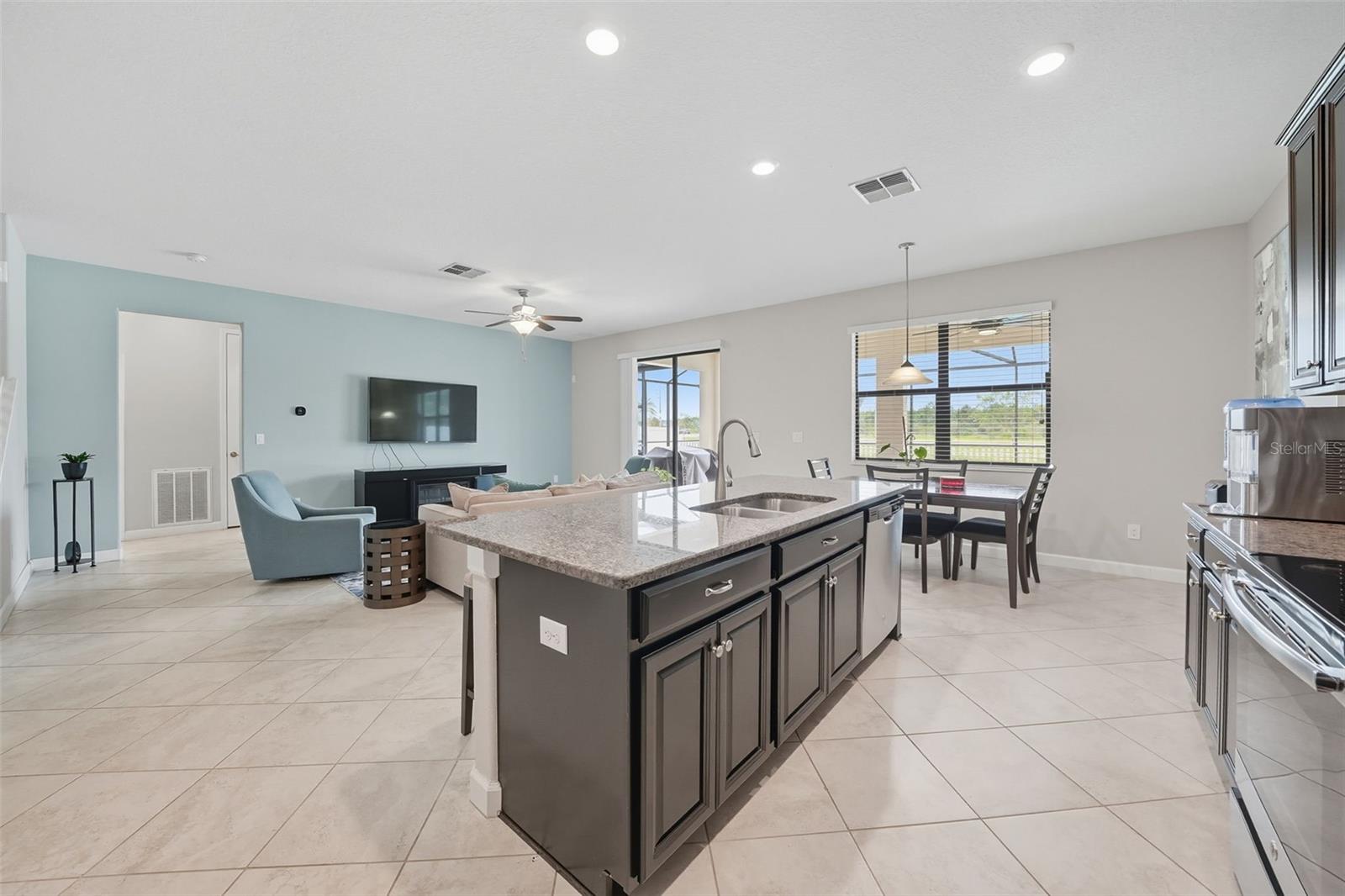 Bright and open layout filled with natural light, featuring an oversized granite island and seamless flow to the dining and living areas. Large windows showcase backyard and pool views