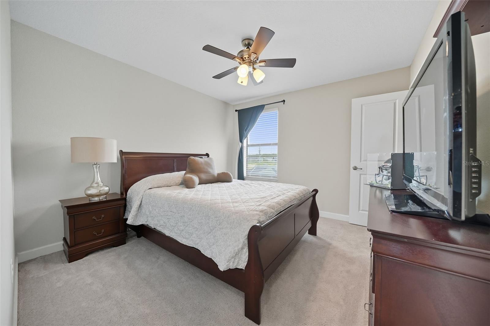 Bright upstairs bedroom with neutral tones, ceiling fan, and plush carpeting—ideal for a guest room, nursery, or personal retreat.