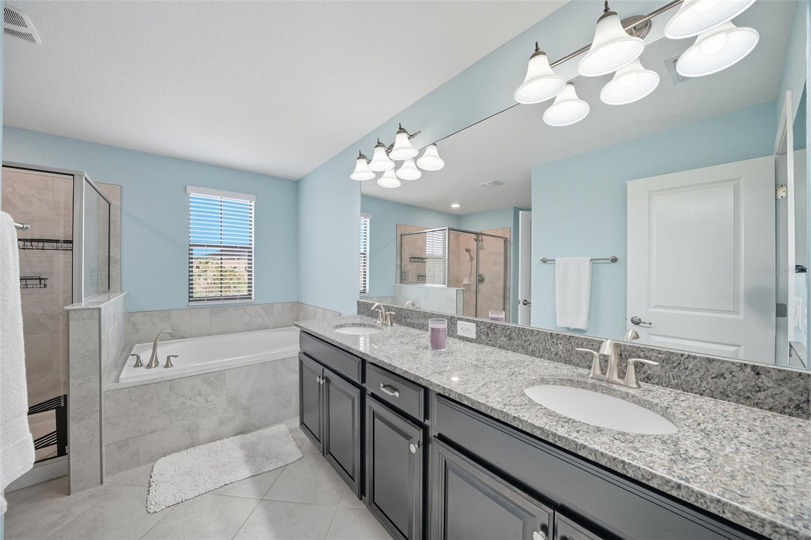 Relax in your spa-like primary bathroom featuring dual granite vanities, a soaking tub, and a walk-in shower