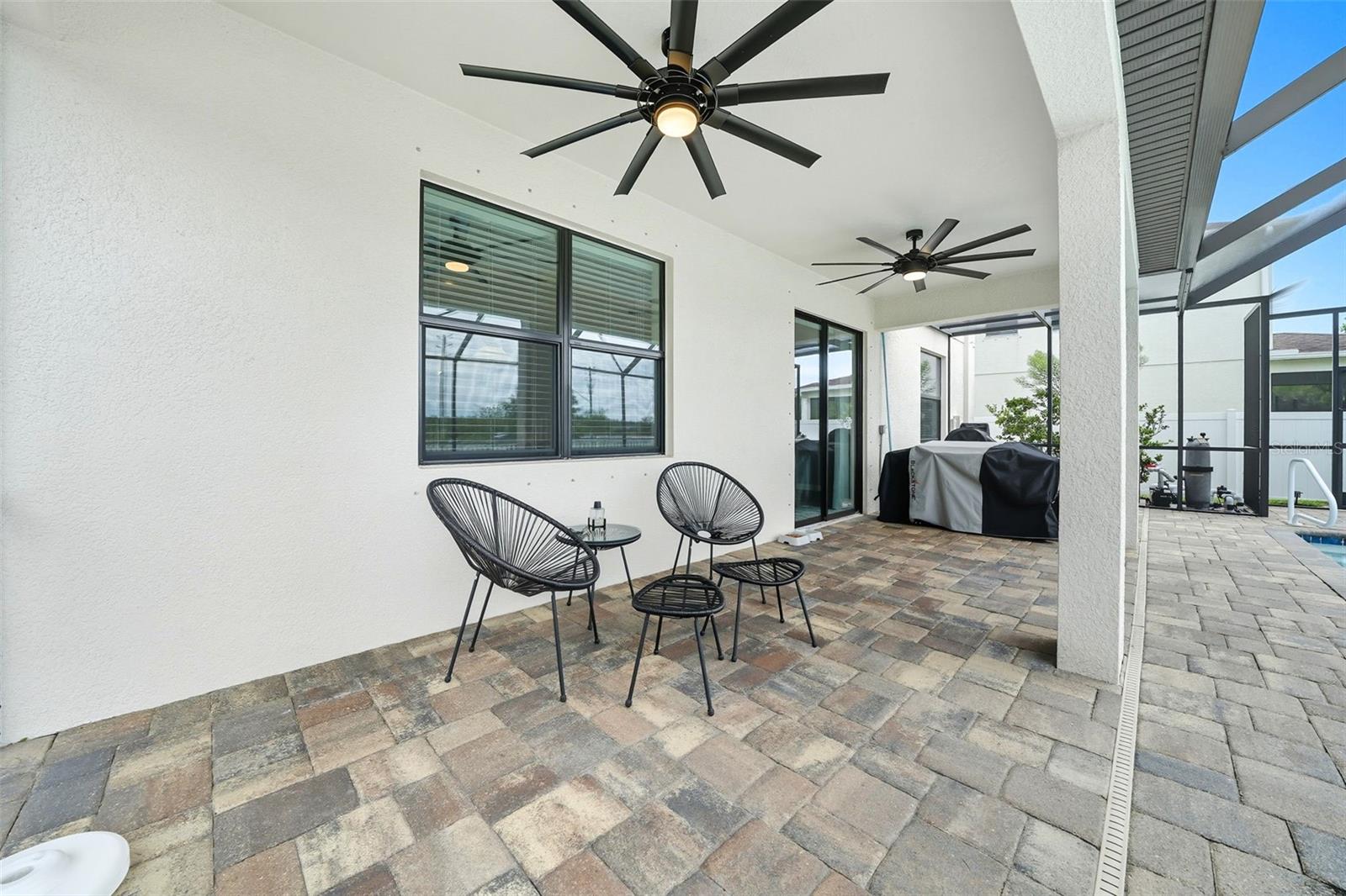Enjoy year-round comfort under the extended covered lanai, complete with dual ceiling fans, paver flooring, and space for both lounging and grilling—perfect for entertaining by the pool