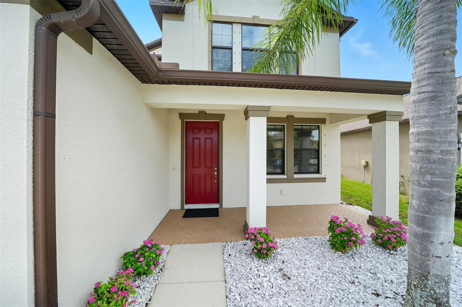 charming covered front porch with fresh landscaping and a bold red door creates a warm welcome for guests. The perfect spot to greet friends and enjoy the neighborhood feel