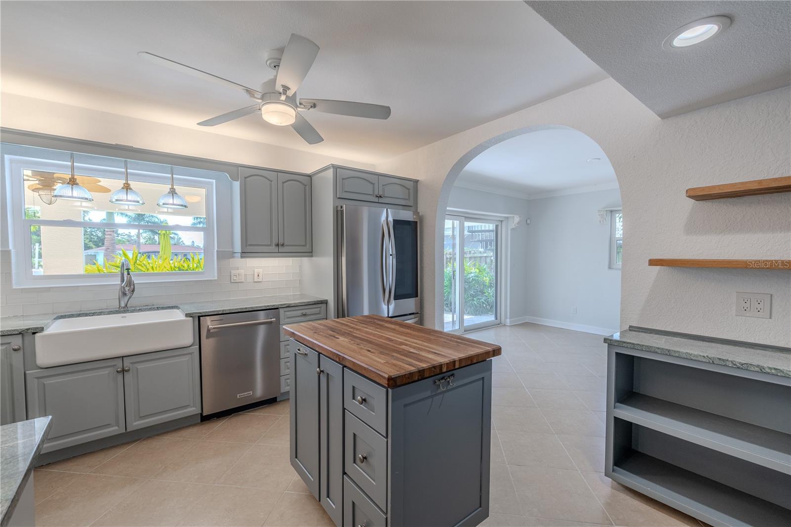 A butcher-block island provides extra prep space, while pendant lighting above the sink and a ceiling fan add both style and comfort. The arched opening leads directly to the dining area and backyard, creating an easy flow for everyday living and entertaining.