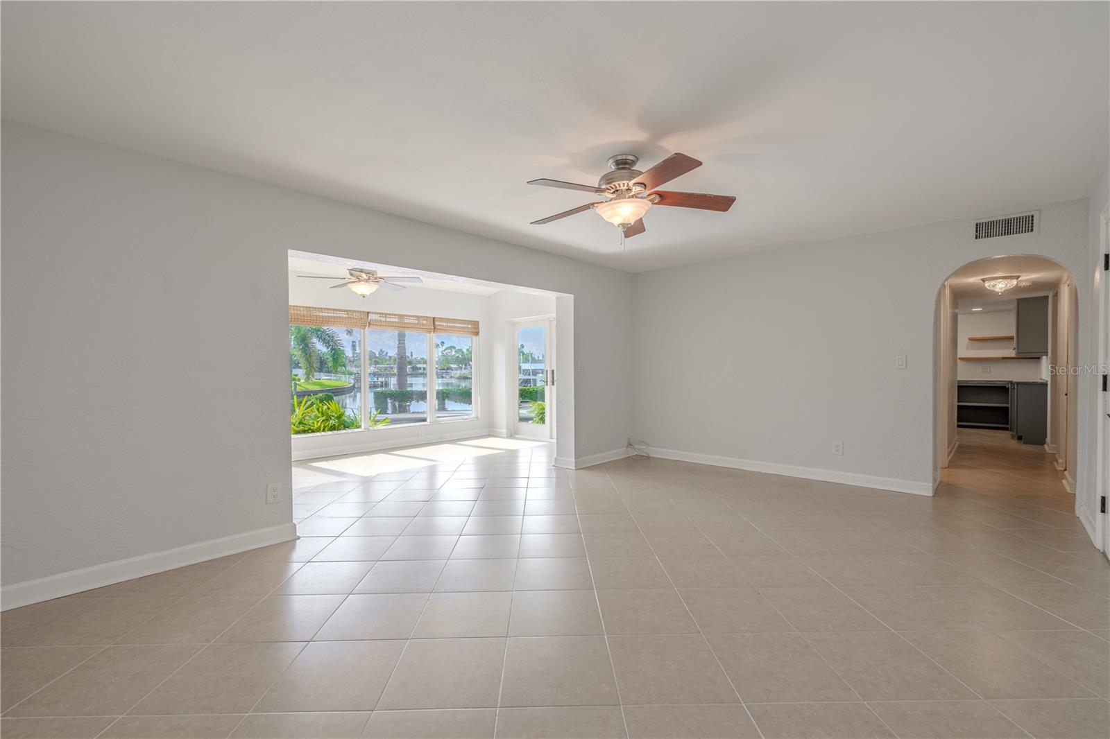 The family room features neutral tile flooring, fresh paint, and a ceiling fan for comfort. The space opens directly to the Florida room, where expansive picture windows frame serene views of the pool and canal, filling both rooms with natural light.