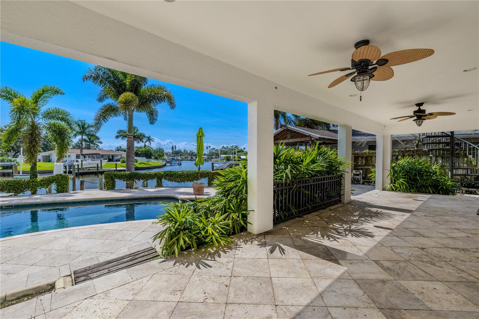 Enjoy year-round outdoor living on the spacious  covered patio, complete with a travertine floor for a timeless, upscale look. Ceiling fans and built-in lighting create comfort and ambiance, making it perfect for everything from relaxing afternoons to nighttime grilling. Overlooking the pool and canal, this shaded retreat seamlessly blends style, function, and waterfront views.