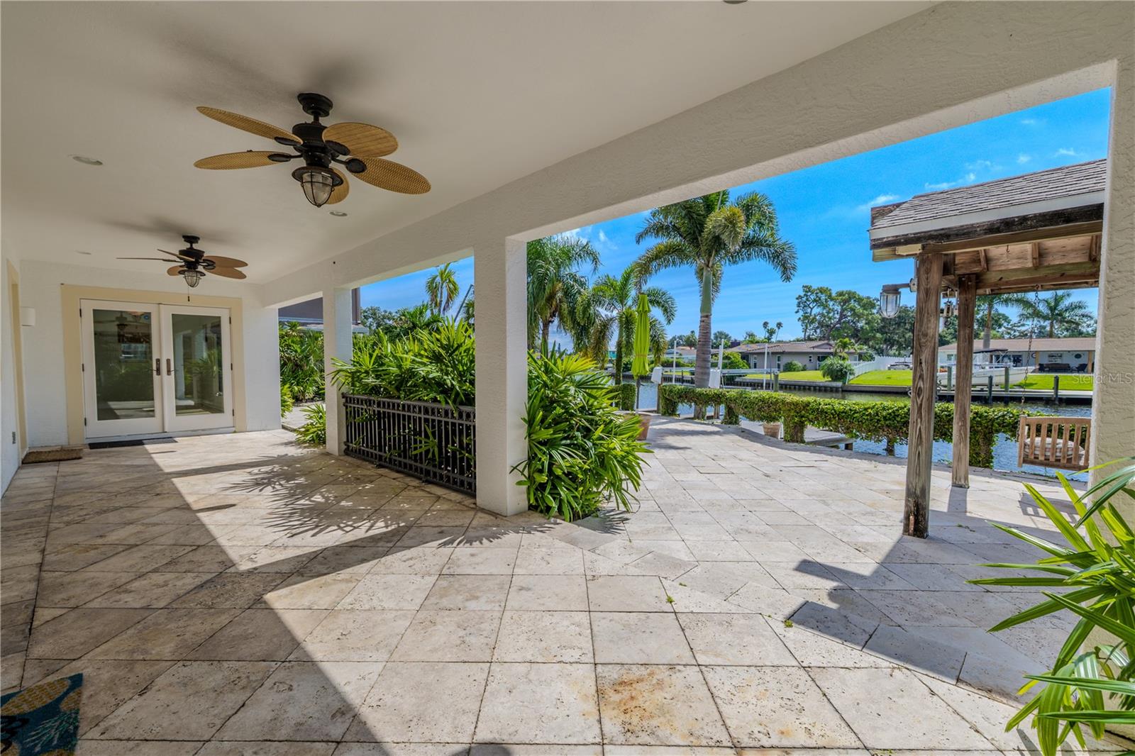 The covered patio with a travertine floor, dual ceiling fans, has built-in lighting for comfort day or night. Framed by lush tropical landscaping, the patio flows seamlessly onto the open pool deck, providing plenty of space for lounging, grilling, and entertaining.