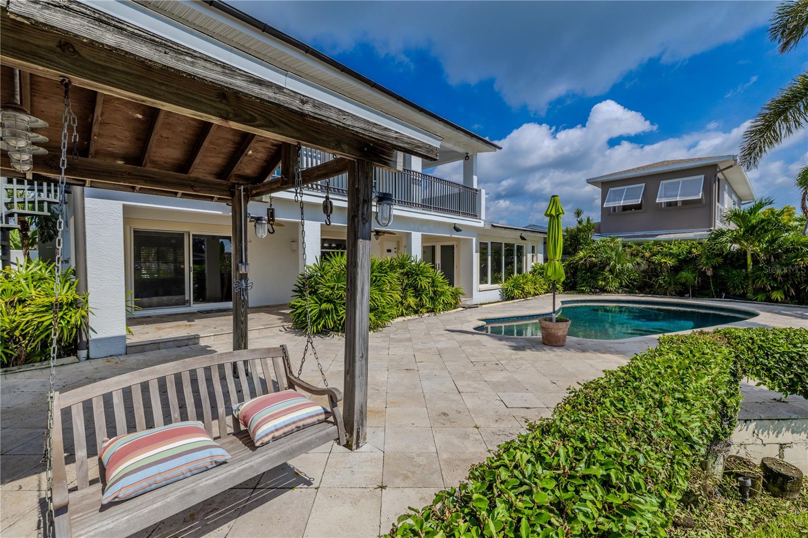 A covered pergola swing with lantern-style lighting creates a cozy retreat overlooking the pool and canal, ideal for morning coffee or sunset views.