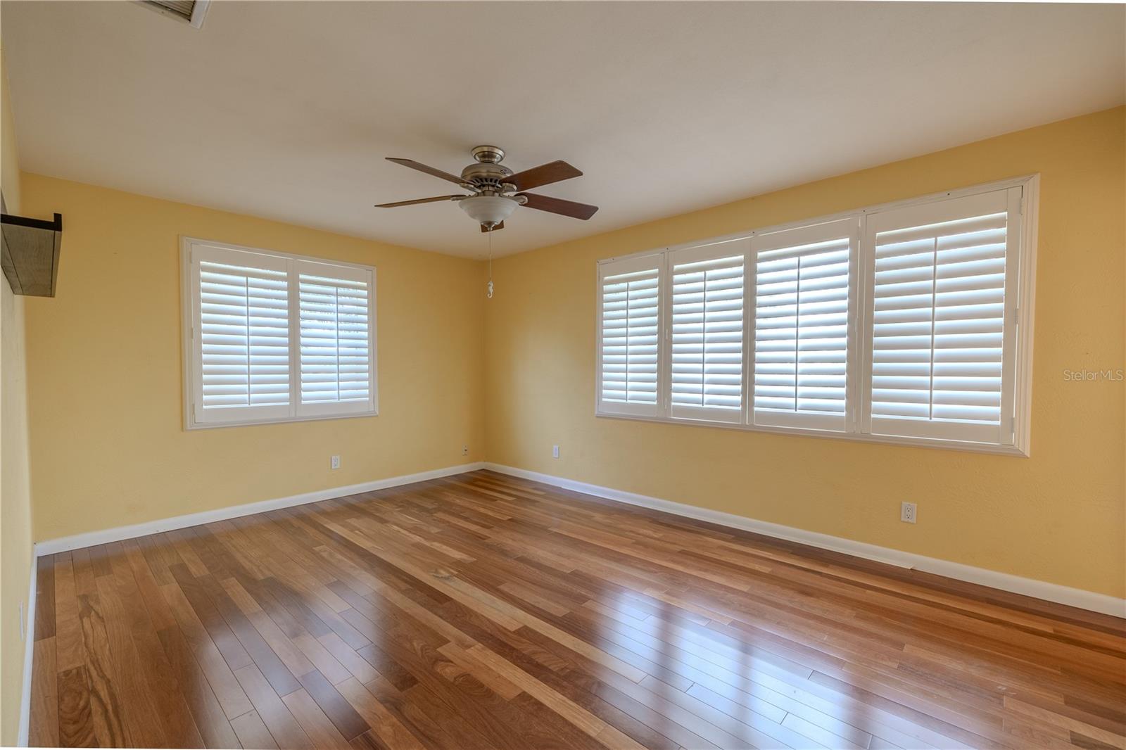 The 2nd bedroom features Brazilian Teak solid wood flooring, custom plantation shutters for privacy and light control, and a ceiling fan with light.