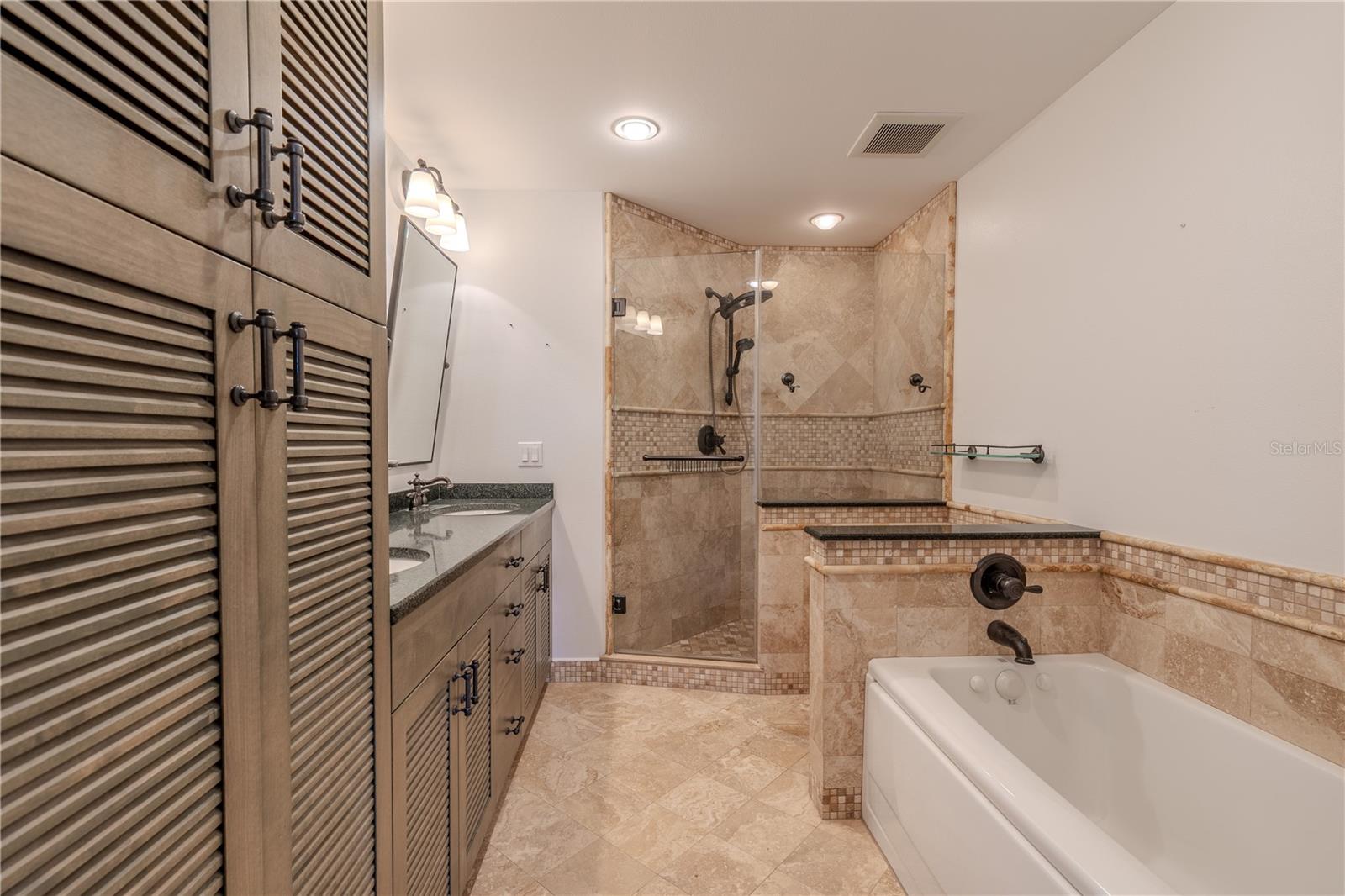 The spa-inspired 3rd/Primary bathroom showcases a travertine floor and walk-in shower, paired with a Cambria quartz countertop and custom deluxe cabinetry with louvered doors for a refined coastal look. A Pearl jetted Jacuzzi tub offers the ultimate in relaxation, while Delta designer plumbing hardware adds both style and function. The dual vanity provides ample storage and convenience, making this bath both luxurious and practical.