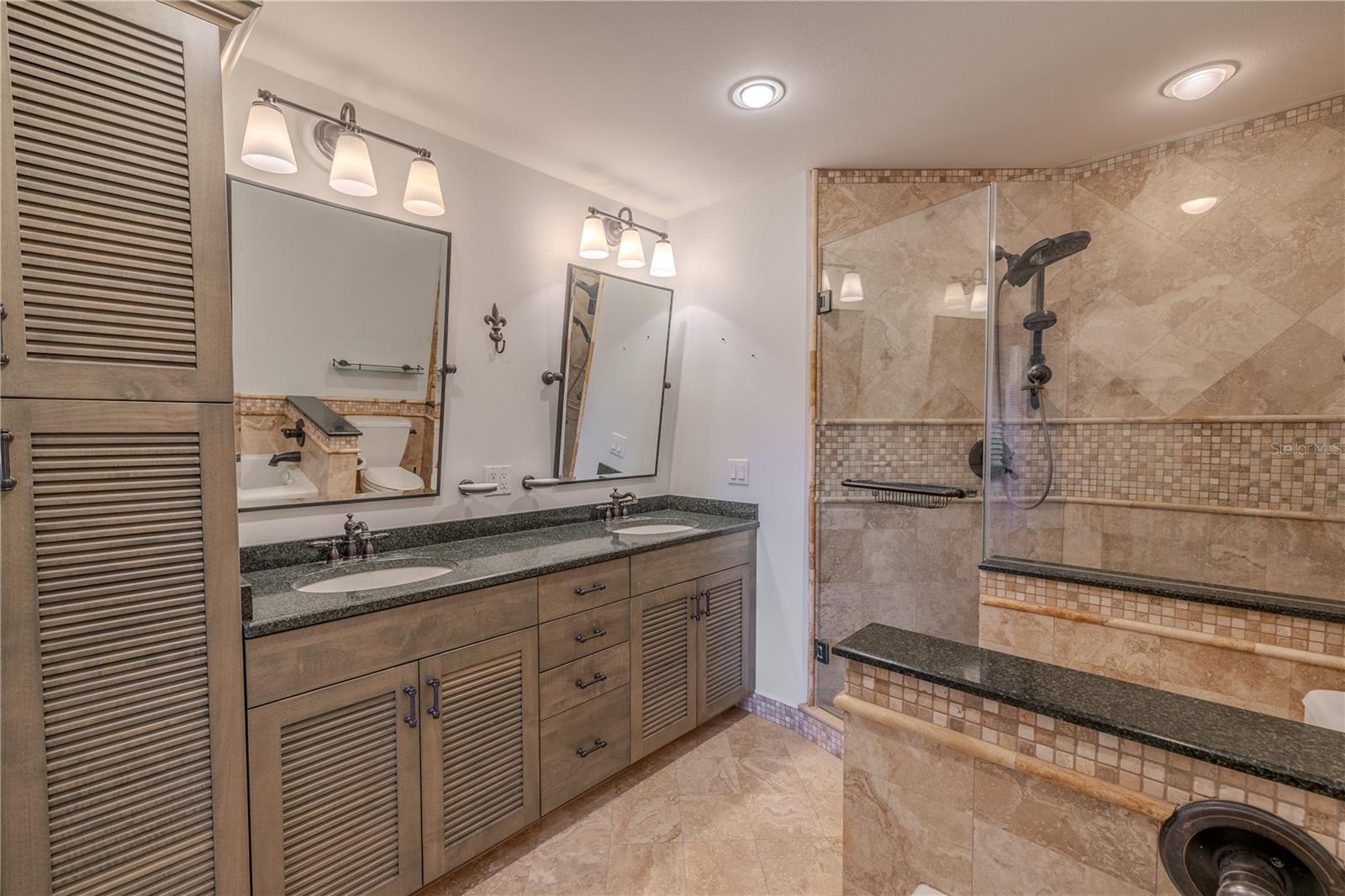 The 3rd/Primary bathroom features a custom deluxe double-sink vanity with Cambria quartz countertops and Delta designer faucets, complemented by rich wood cabinetry with louvered doors for a timeless coastal touch. Ample storage continues with a matching built-in linen closet, give both beauty and functionality while keeping the space organized.