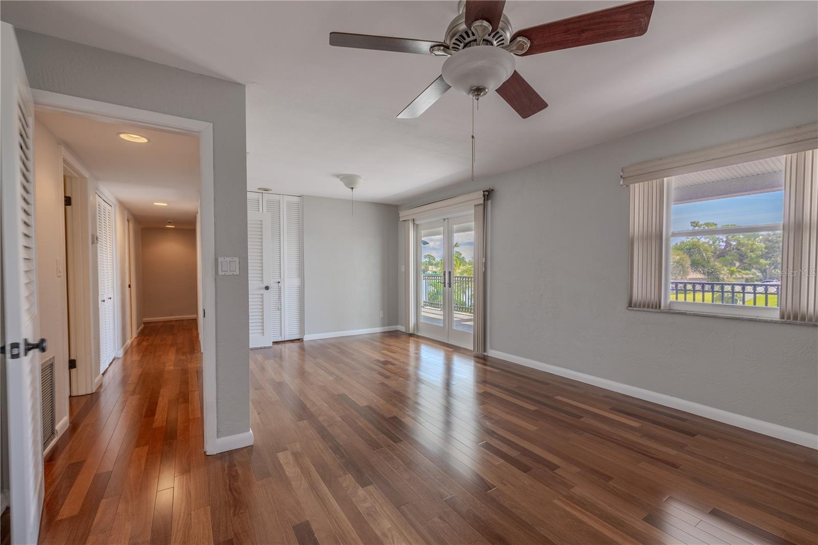 The spacious primary bedroom showcases Brazilian Teak solid wood flooring, soft neutral walls, and abundant natural light from multiple windows. Sliding glass doors open directly onto the expansive 330 sq. ft. upper balcony, creating a seamless indoor-outdoor retreat with serene views.
