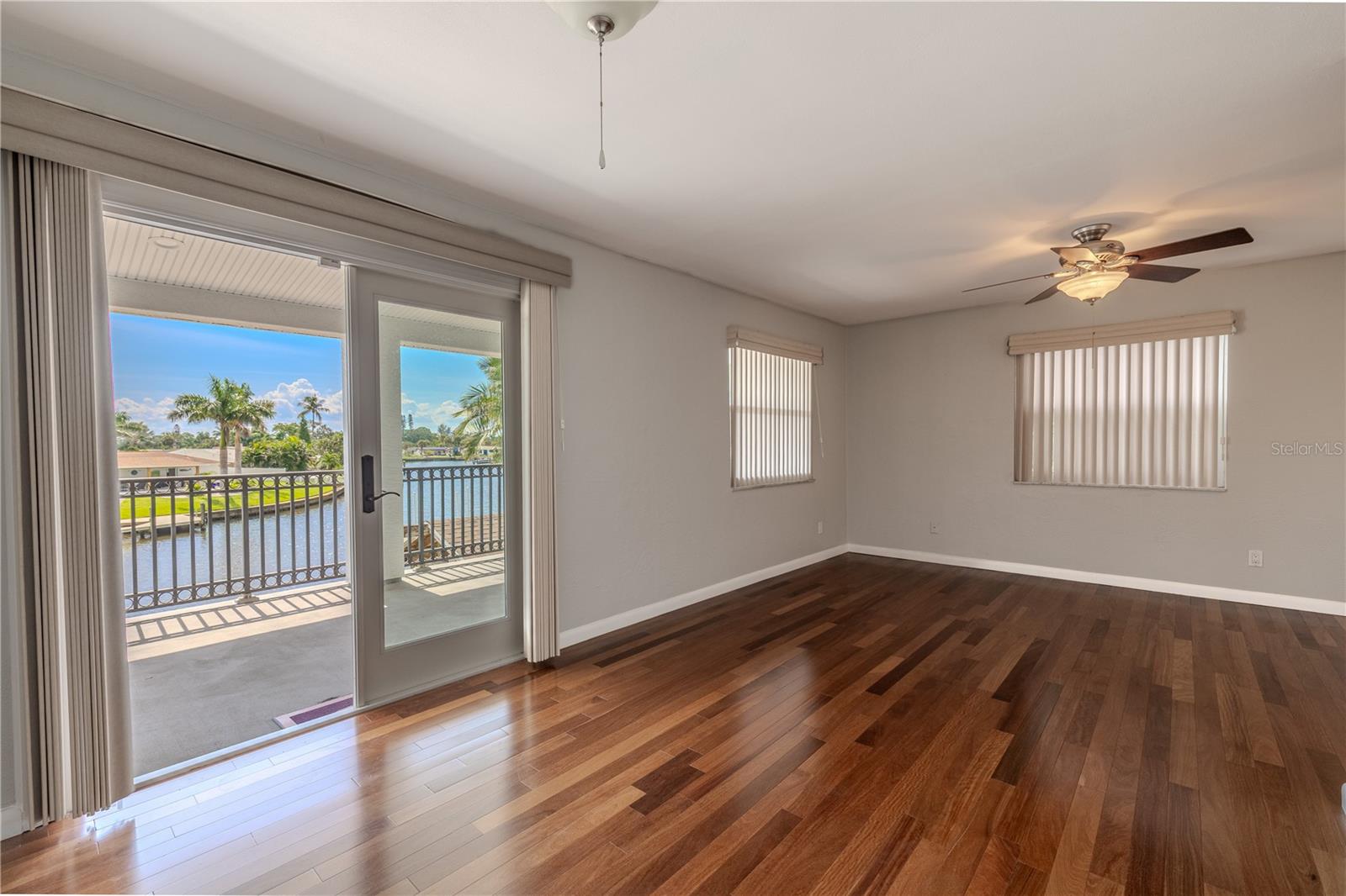 The spacious primary bedroom showcases Brazilian Teak solid wood flooring and abundant natural light through multiple (triple paned and hurricane rated) windows and sliding glass doors. The room opens directly onto the expansive 330 sq. ft. upper balcony, offering sweeping waterfront views and a seamless indoor-outdoor connection.