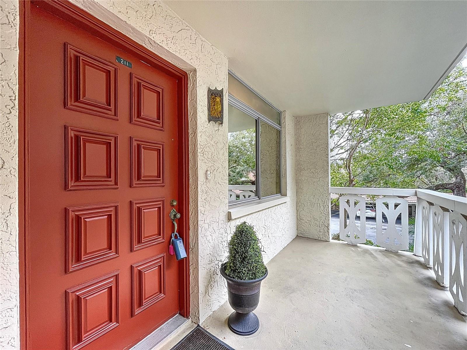 Welcoming front entry features a bold red door and private covered balcony, offering a peaceful space to enjoy fresh air and leafy views.