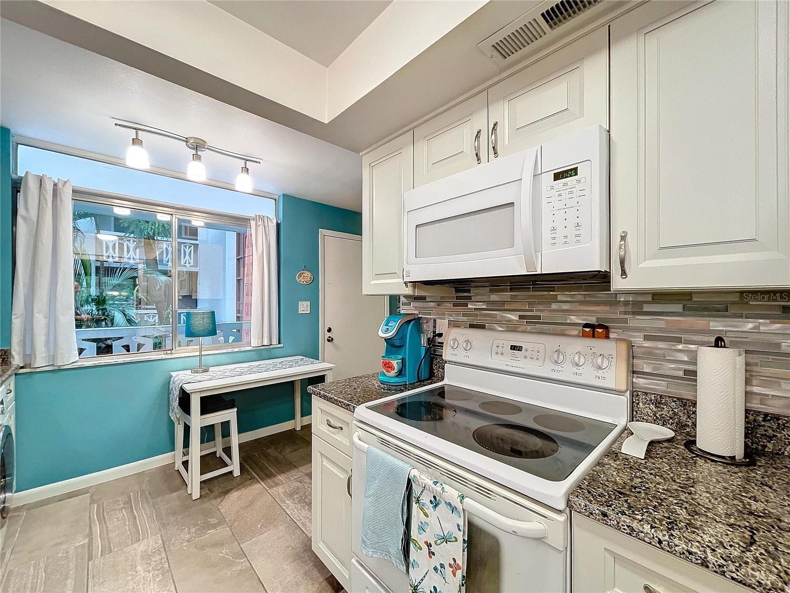 Equipped with a white electric range, built-in microwave, and adjacent coffee station, all framed by neutral tones and clean lines.