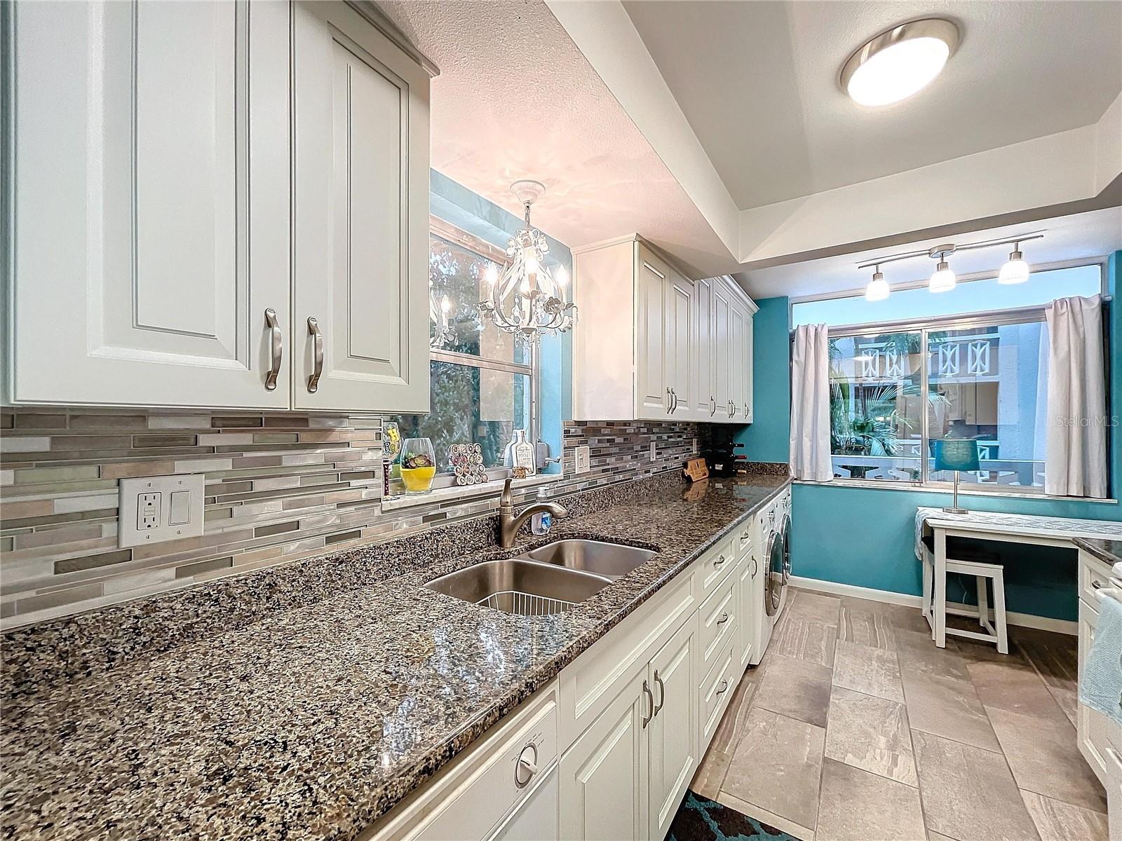 A large window above the sink brings in natural light, while the dual basin sink and elegant chandelier add functionality and flair.